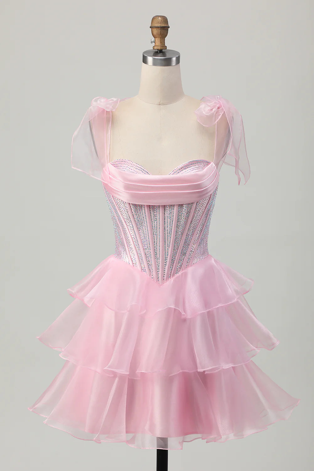 Model wearing a pink A-line tiered beaded short homecoming dress with a corset bodice and bow straps.