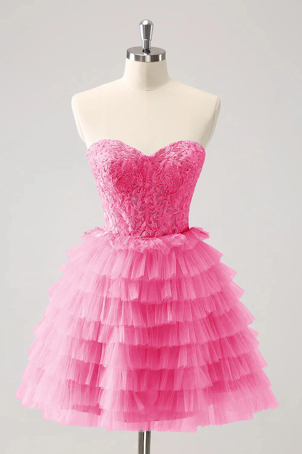 Model wearing a pink A-line formal gown with sweetheart neckline and tiered skirt.