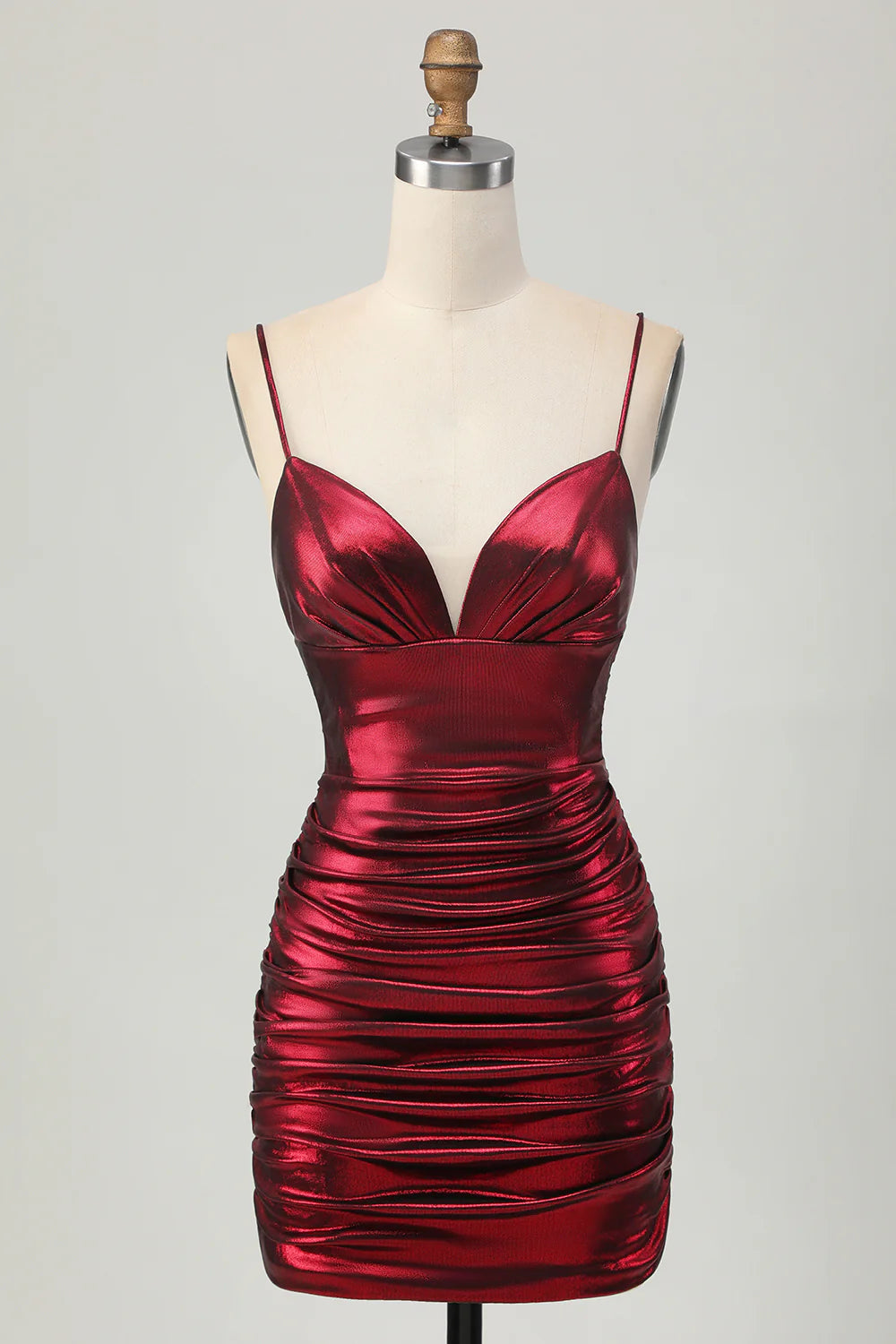 Model wearing a metallic burgundy ruched satin short homecoming dress with spaghetti straps.