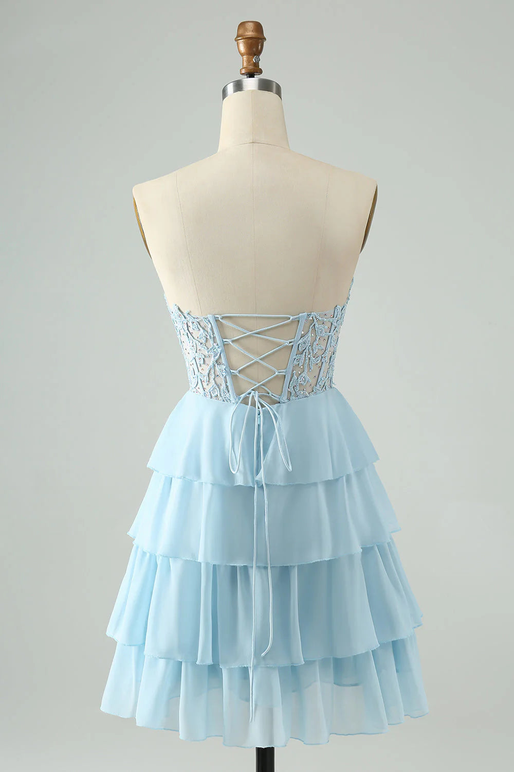 Model wearing a light blue sweetheart tiered short homecoming dress, side view.