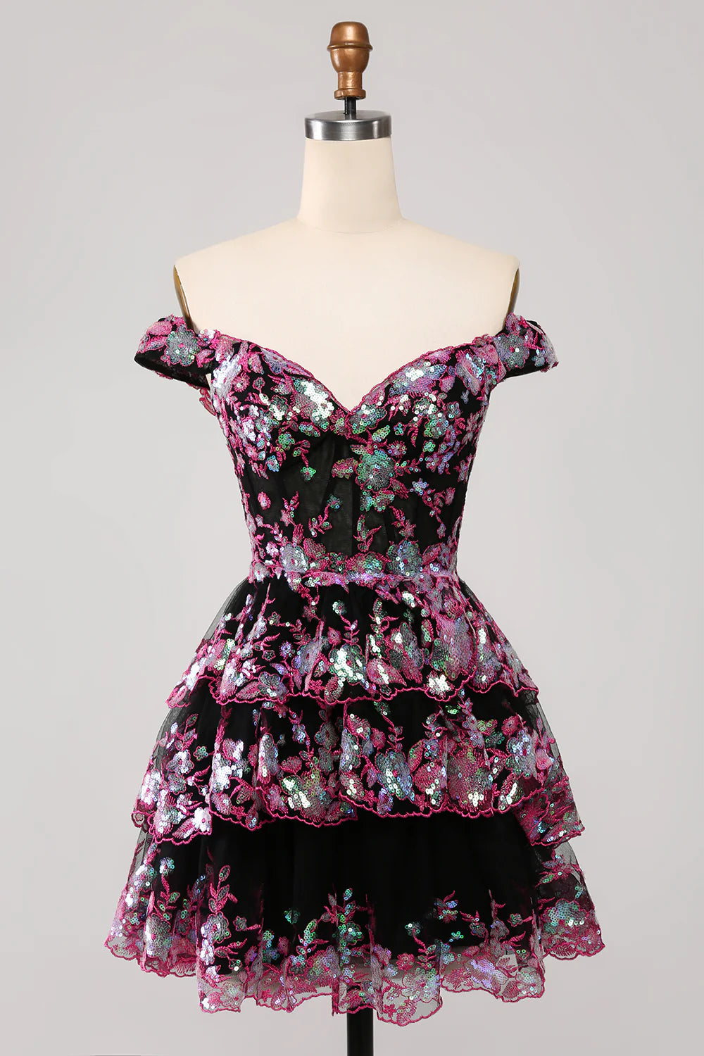 Model wearing a sparkly black and pink A-line off-shoulder short homecoming dress with a tiered skirt.