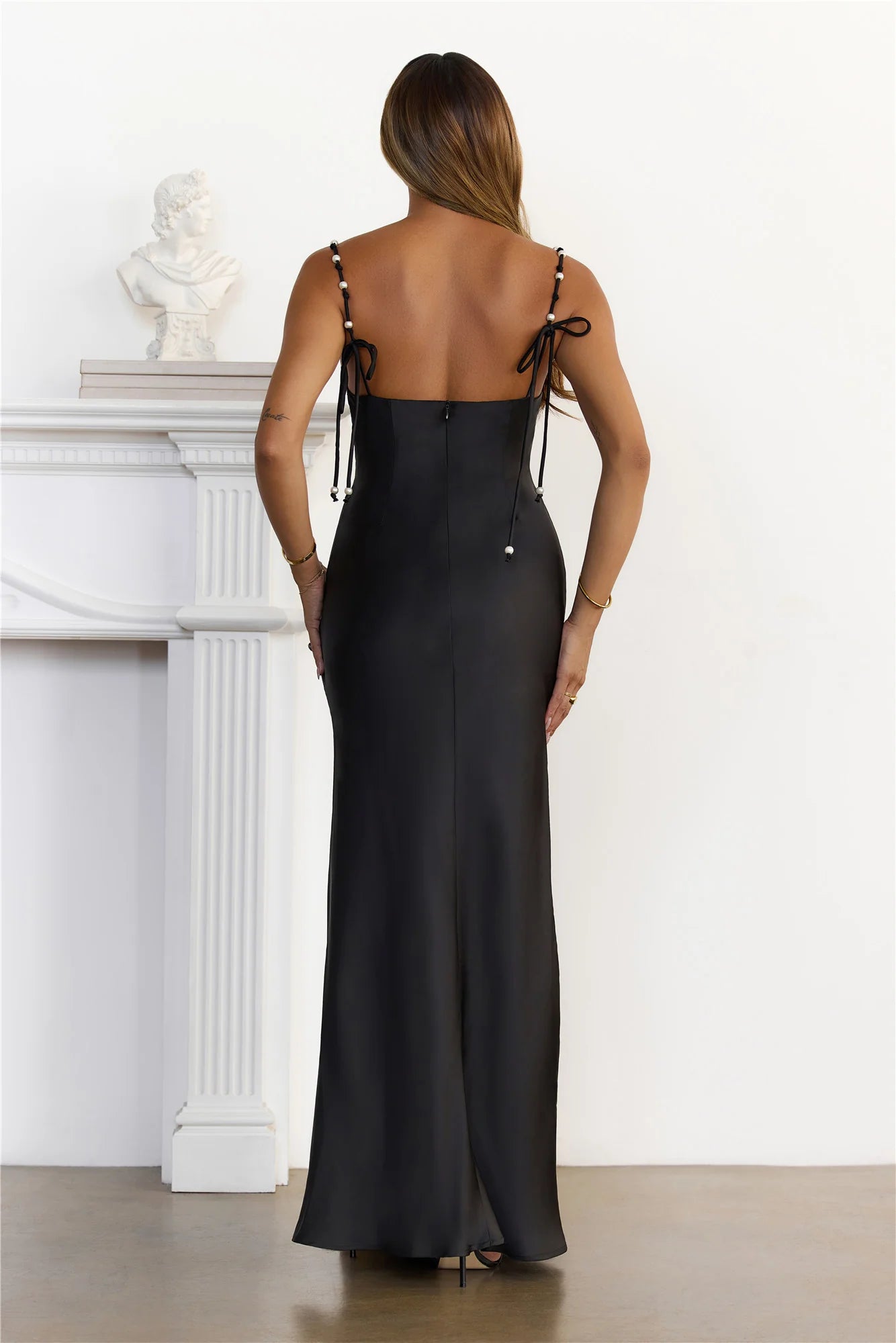 Stunning Black Satin Maxi Dress adorned with delicate pearl beaded spaghetti straps, a romantic sweetheart neckline, a flattering high slit, and an elegant open back with tie detail.