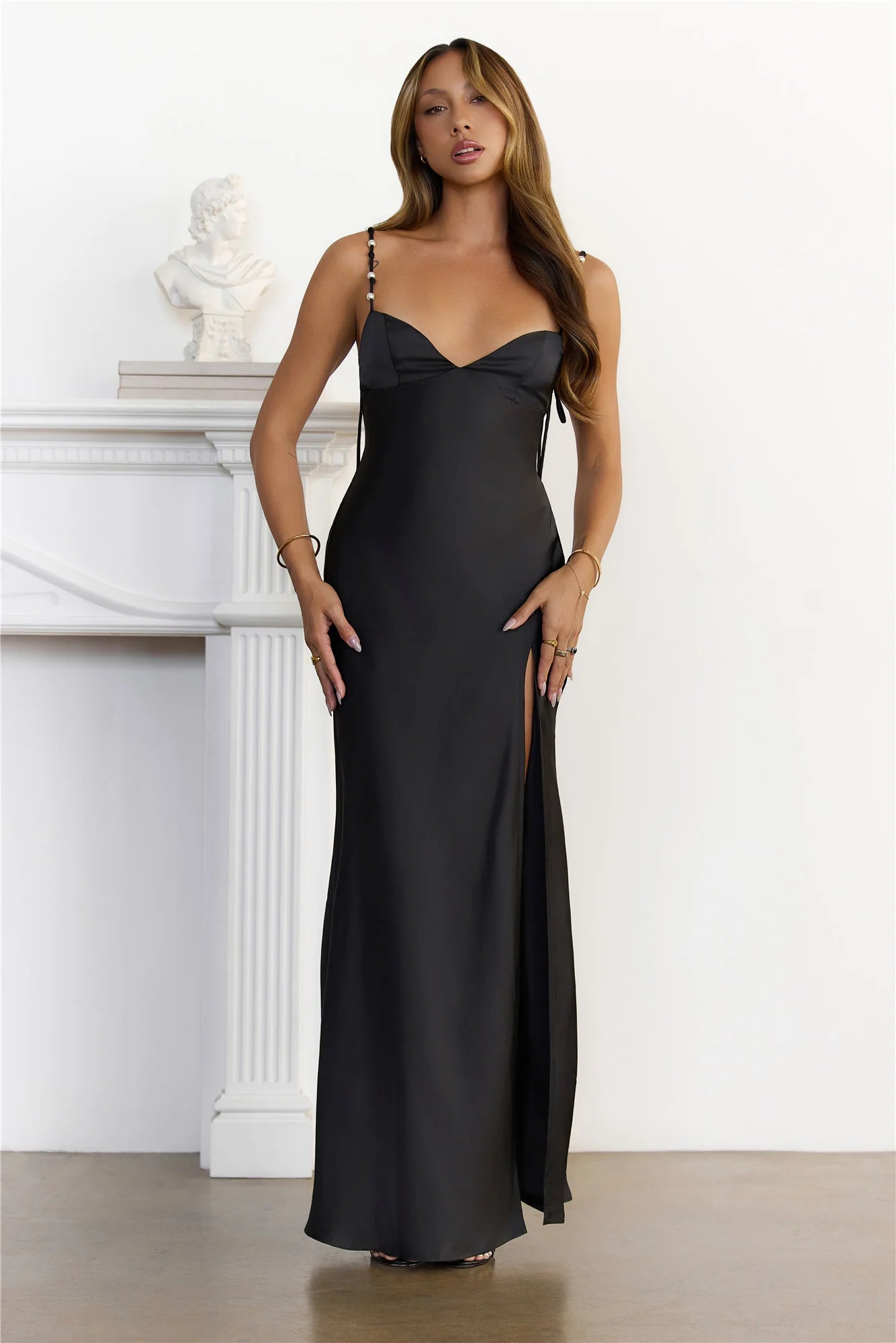 Stunning Black Satin Maxi Dress adorned with delicate pearl beaded spaghetti straps, a romantic sweetheart neckline, a flattering high slit, and an elegant open back with tie detail.