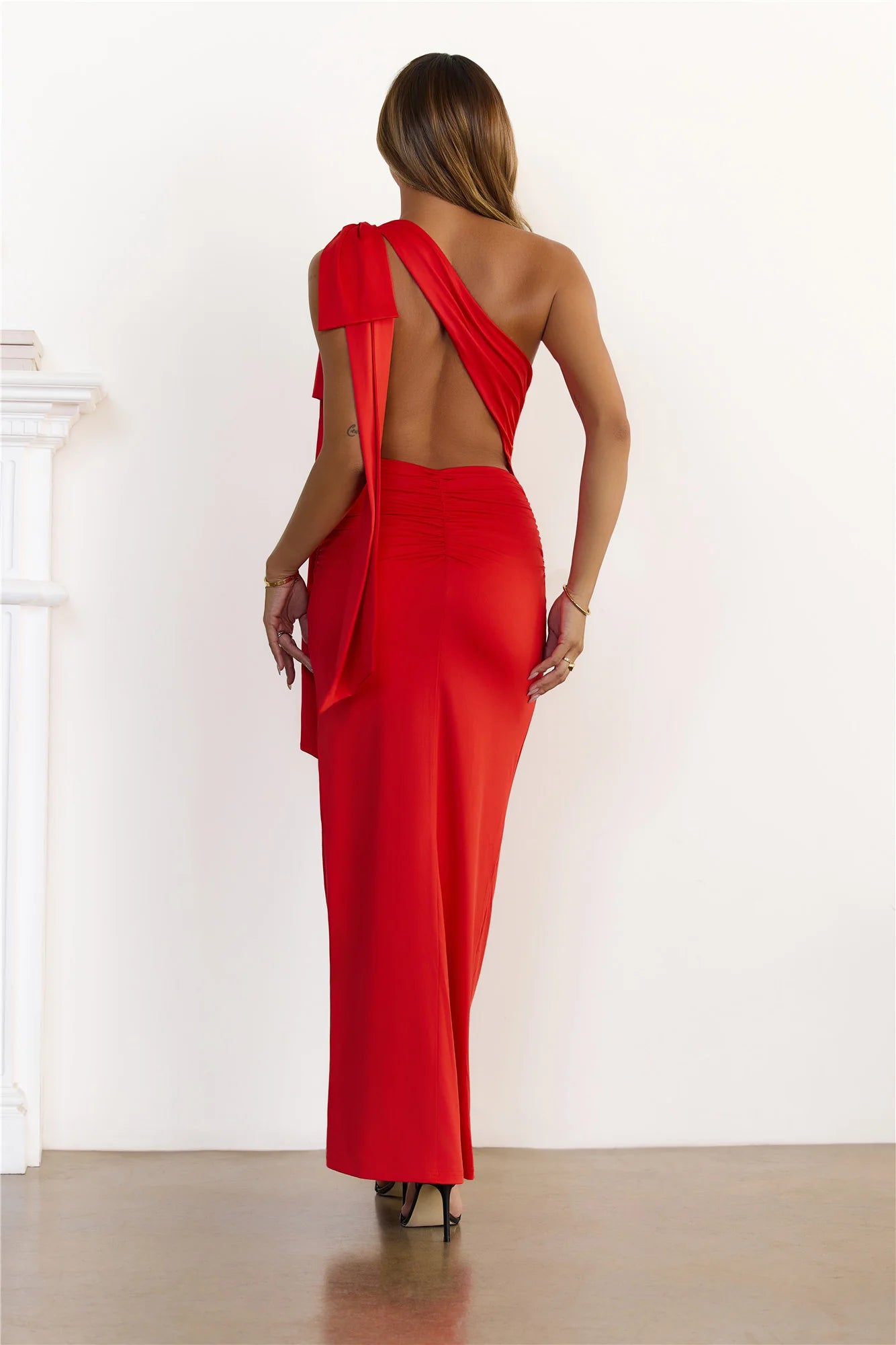 Stunning glamorous red one-shoulder maxi dress featuring an elegant draped sash, a flattering open back design, and delicate ruching at the waist for a beautifully tailored silhouette.
